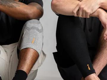 To som sitter på gulvet, den ene med Knee Sleeve og sokker, den andre med Leg Sleeves