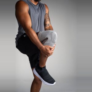 Grå Knee Sleeve på en mann som holder kneet opp mot brystet